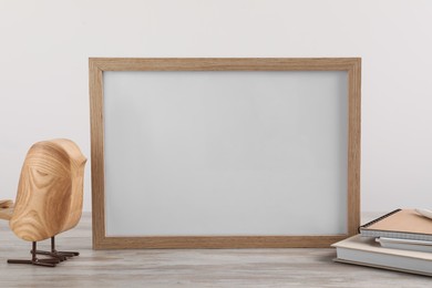 Blank photo frame, notebooks and decorative bird on wooden table