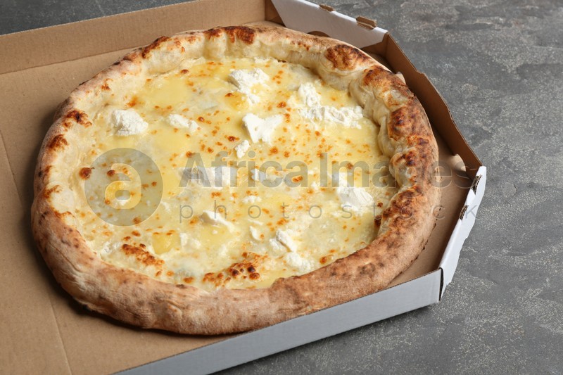 Photo of Delicious hot cheese pizza in takeout box on grey table