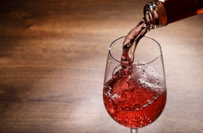 Pouring rose wine from bottle into glass on wooden table, closeup. Space for text