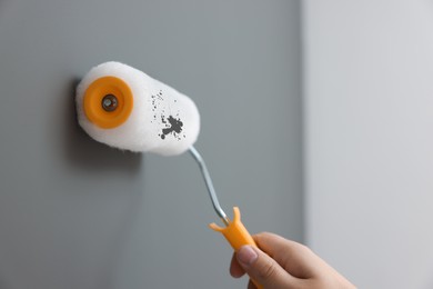 Photo of Worker using roller to paint wall with grey dye indoors, closeup