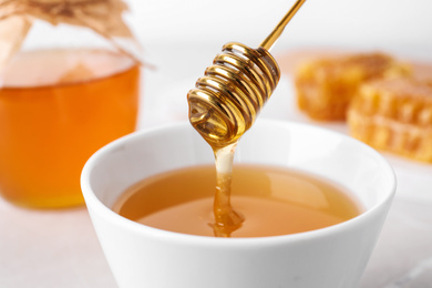 Photo of Dripping tasty honey from dipper into bowl on table, closeup