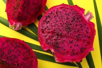 Photo of Delicious cut red pitahaya fruit with palm leaf on yellow background, flat lay