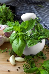 Photo of Mortar with different fresh herbs near garlic, horseradish roots and black peppercorns on wooden table