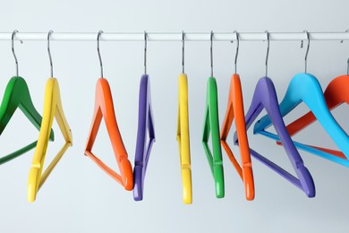 Bright clothes hangers on metal rail against light background