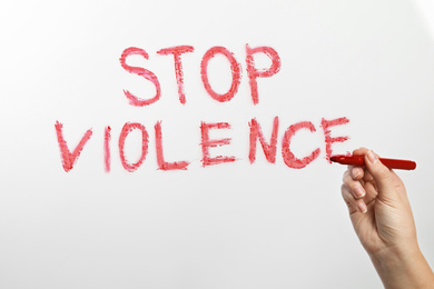 Woman writing phrase STOP VIOLENCE on glass against white background, closeup