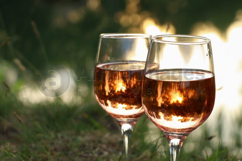 Glasses of tasty rose wine on blurred background, closeup and space for text. Picnic season