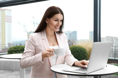 Businesswoman with laptop and coffee in outdoor cafe. Corporate blog