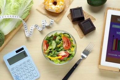 Photo of Tablet with weight loss calculator application, tasty salad and other food on wooden table, flat lay