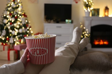 Photo of Woman with popcorn watching TV in room decorated for Christmas, closeup