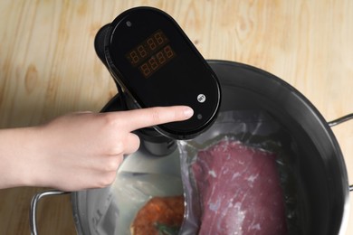 Woman using thermal immersion circulator at wooden table, closeup. Sous vide, cooking meat in vacuum packing
