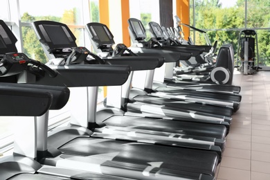 Gym interior with row of treadmills near windows