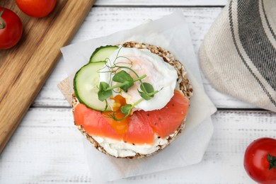Crunchy buckwheat cakes with salmon, poached egg and cucumber slices on white wooden table, flat lay