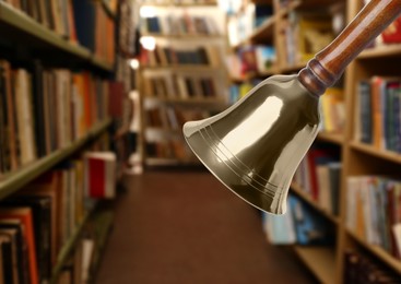 Golden school bell with wooden handle and blurred view of books on shelves in library