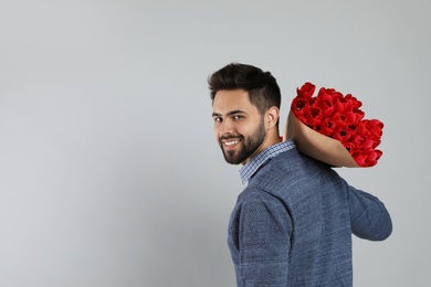Happy man with red tulip bouquet on light grey background, space for text. 8th of March celebration