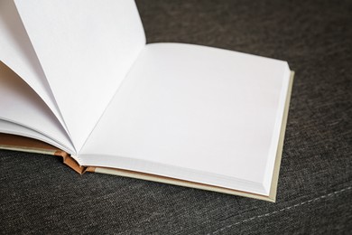Open blank book on grey sofa, closeup view