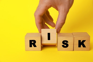Man making word Risk with wooden cubes on yellow background, closeup