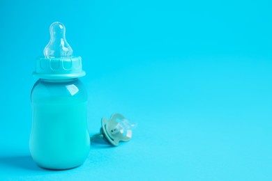 Photo of One feeding bottle with milk and pacifier on light blue background. Space for text