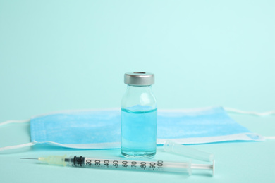Vial, syringe and surgical mask on turquoise background. Vaccination and immunization