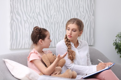 Young female psychologist working with little child in office