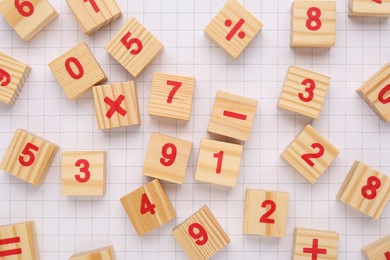 Photo of Wooden cubes with mathematical symbols and numbers on sheet of grid paper, flat lay