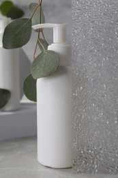 Photo of Face cleansing product and eucalyptus leaves on light grey table