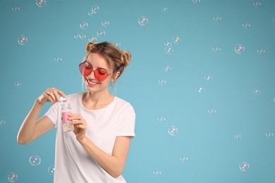Young woman blowing soap bubbles on light blue background, space for text