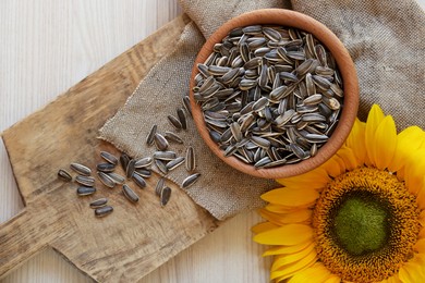 Photo of Organic sunflower seeds and flower on wooden table, flat lay