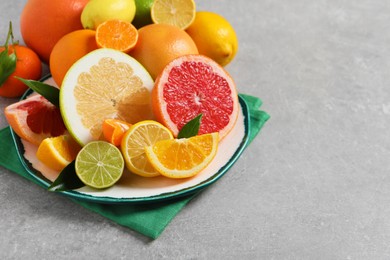 Photo of Plate with different citrus fruits and fresh leaves on light grey table. Space for text