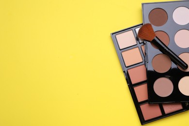 Photo of Different contouring palettes and brush on yellow background, flat lay with space for text. Professional cosmetic product