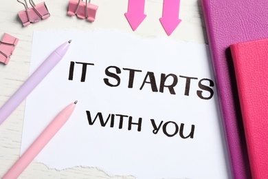 Sheet of paper with phrase It Starts With You and stationery on white table, flat lay
