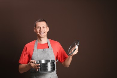 Happy man with cooking pot on brown background. Space for text