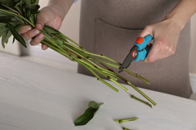 Florist cutting stems of flowers with pruner at workplace, closeup