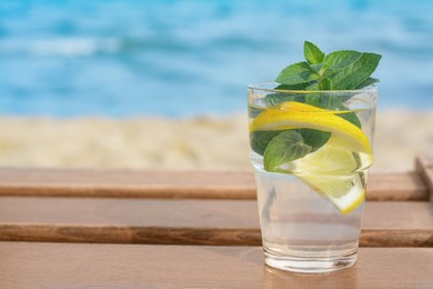 Refreshing water with lemon and mint on wooden table outdoors, space for text