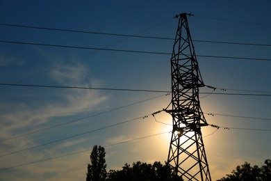 Silhouettes of high voltage tower and trees in evening