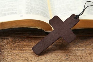 Christian cross and Bible on wooden table, closeup