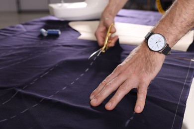 Photo of Professional tailor cutting fabric by following chalked sewing pattern at table, closeup