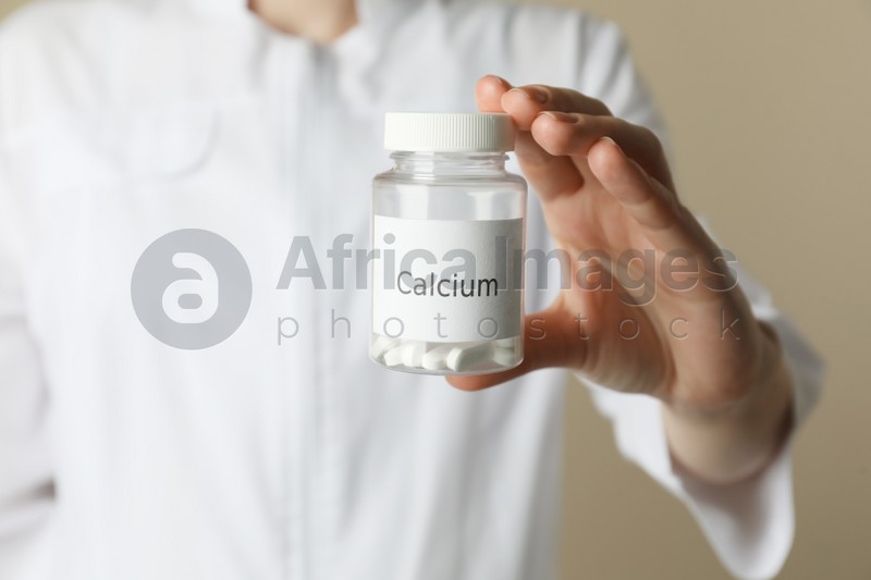 Calcium supplement. Doctor holding bottle with pills on beige background, closeup