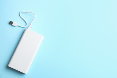 Modern portable charger with cable on light blue background, top view. Space for text