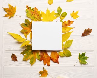 Photo of Autumn leaves and blank card on white wooden table, flat lay. Space for text