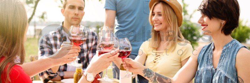 Young people with glasses of wine at table outdoors. Banner design