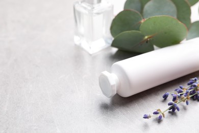 Tube of hand cream, eucalyptus branch and lavender on light grey table, space for text