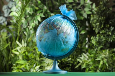 Photo of Globe in plastic bag on table against green leaves. Environmental conservation