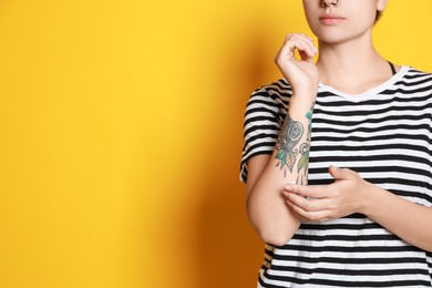 Woman applying cream on her arm with tattoos against yellow background, closeup. Space for text
