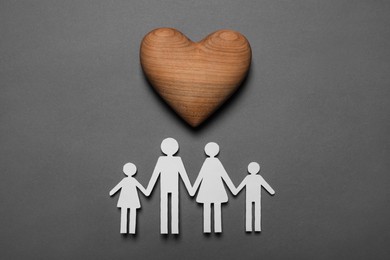 Paper family figures and wooden heart on grey background, flat lay. Insurance concept