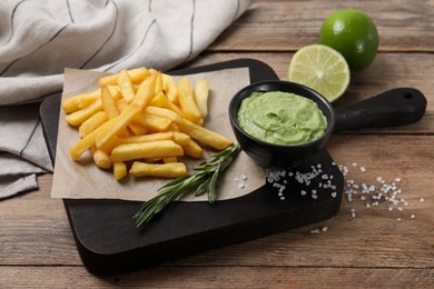 Serving board with french fries, avocado dip, rosemary and lime served on wooden table
