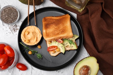 Delicious sandwich with hummus and vegetables, ingredients on white textured table, flat lay