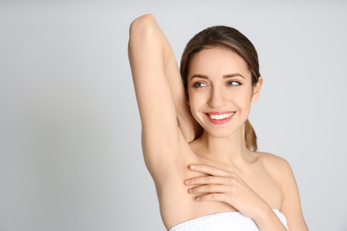 Young woman showing armpit with smooth clean skin on light grey background