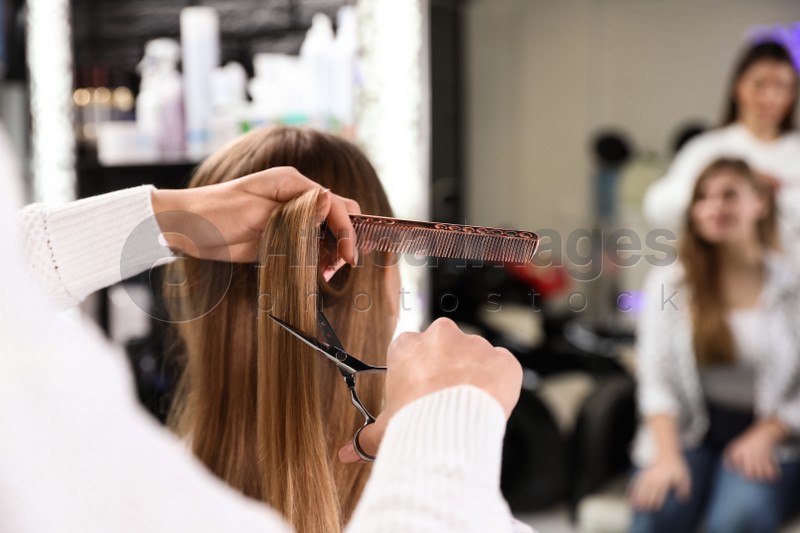 Hairdresser making stylish haircut with professional scissors in salon, closeup