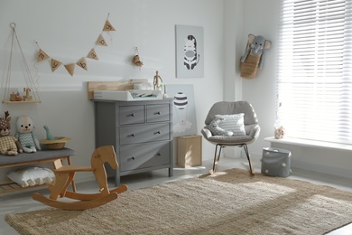 Beautiful baby room interior with toys, rocking chair and modern changing table