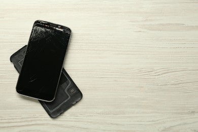 Damaged smartphone on wooden background, flat lay with space for text. Device repairing